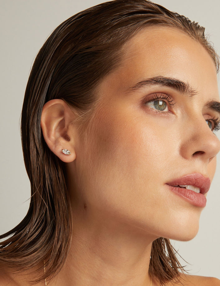 Model. Close up of woman wearing a marquise shaped diamond stud earring on a beige background.