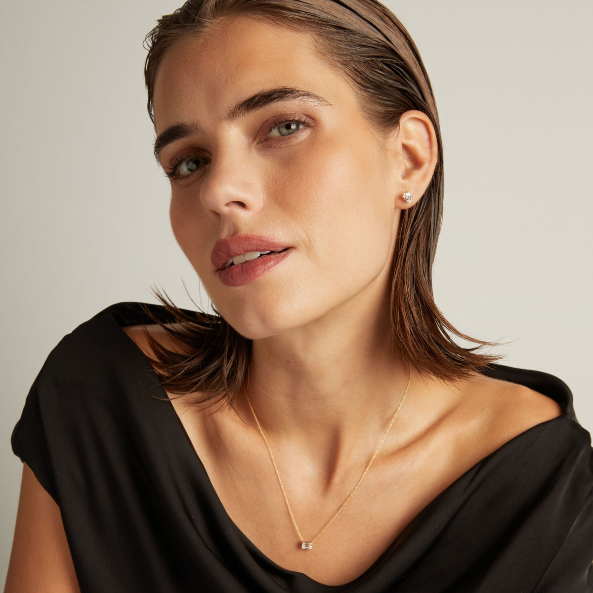 Model. Close up of woman wearing an oval diamond stud earring on a beige background.