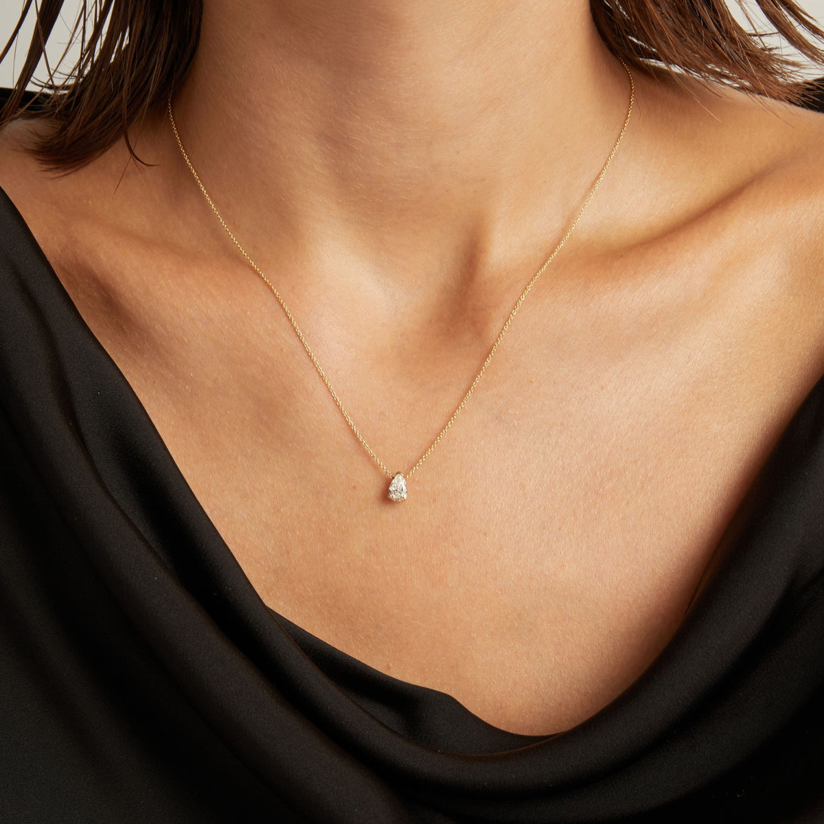 Model. Close up of woman wearing a black top with a pear diamond solitaire necklaces on a beige background.