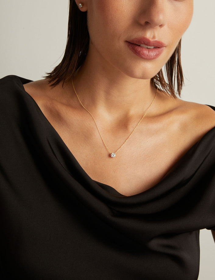 Model. Close up of woman wearing a black top with a round shaped diamond solitaire necklaces on a beige background. 