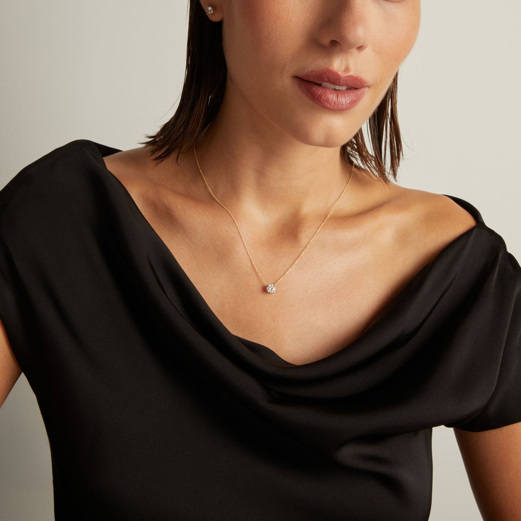 Model. Close up of woman wearing a black top with a round shaped diamond solitaire necklaces on a beige background. 