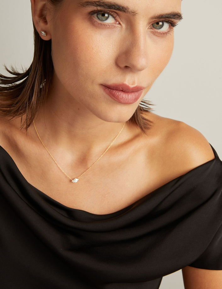 Close up of woman wearing a black top with a marquise shaped diamond solitaire necklaces on a beige background.