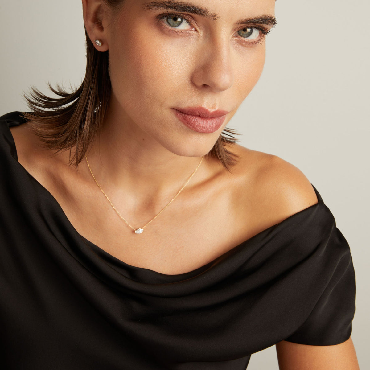 Close up of woman wearing a black top with a marquise shaped diamond solitaire necklaces on a beige background.