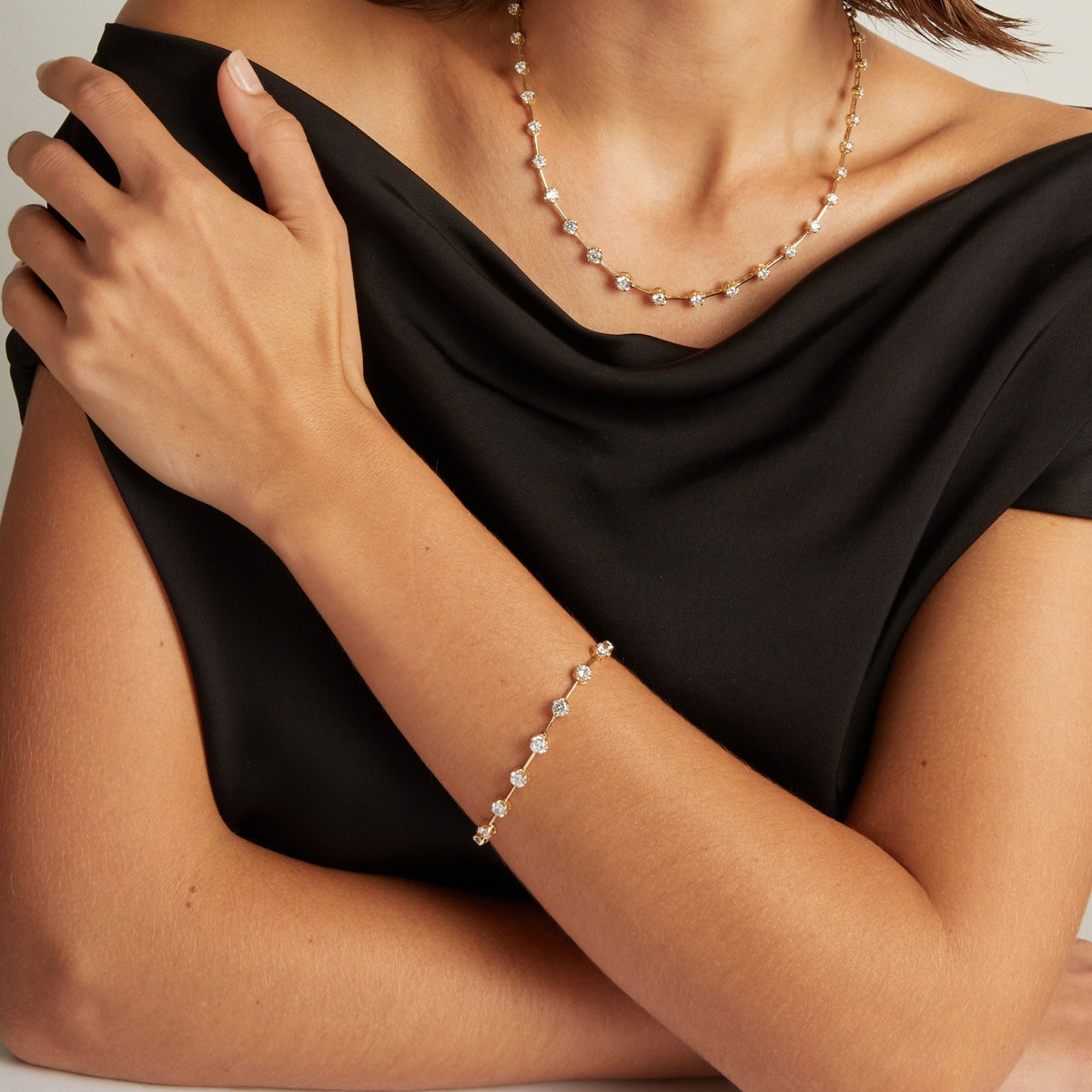 Model. Close up of woman wearing a black shirt with a diamond bar bracelet and necklace on beige background.