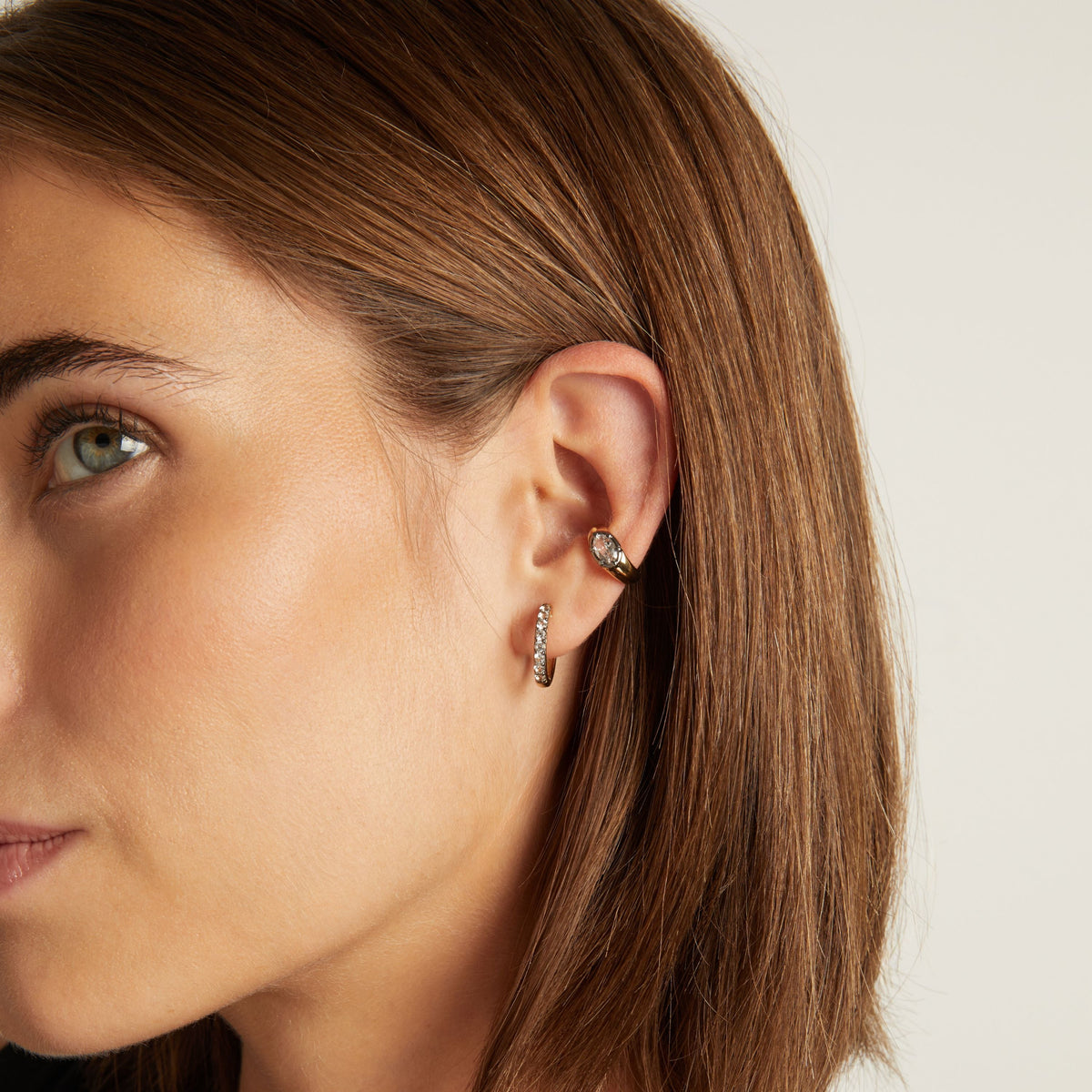 Model. Close up of woman wearing black rhodium huggie earring and a bold ear cuff on neutral background.