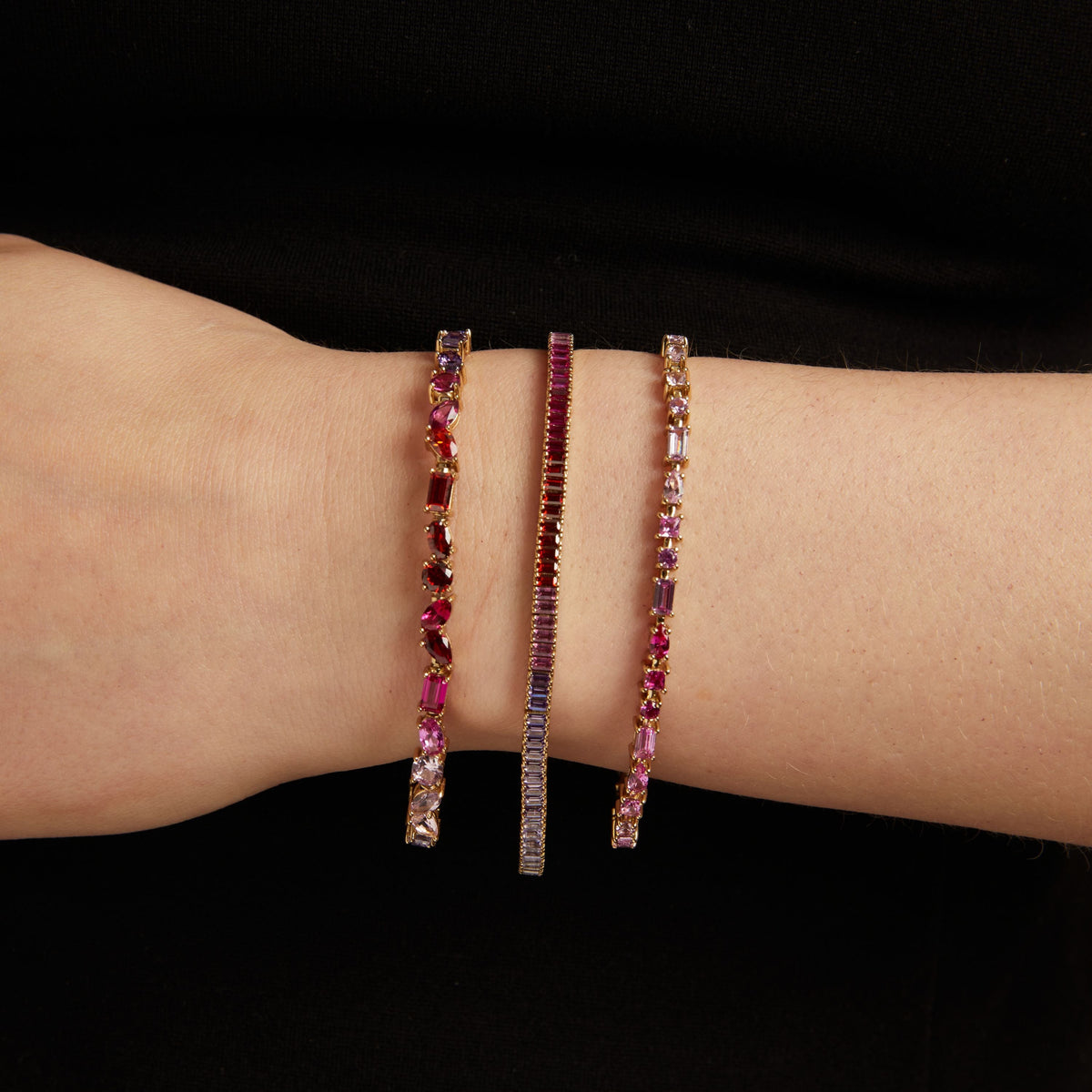 Model. 3 colorful tennis bracelets on a person's wrist against a black background.