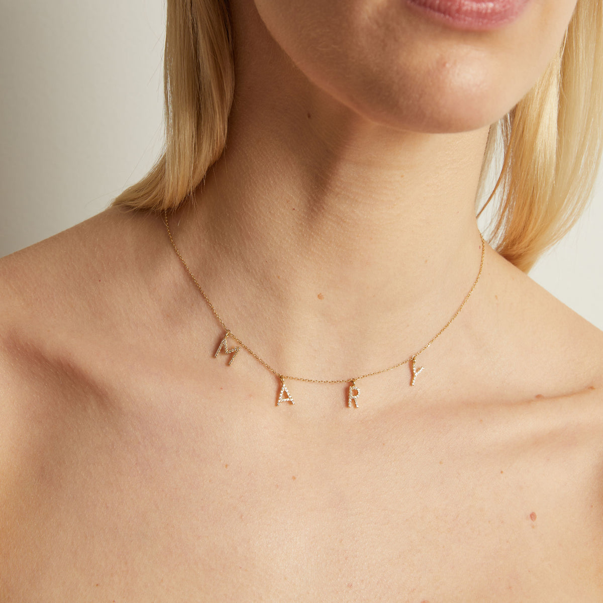 Model. Gold necklace with letter pendants on a person's neck against a neutral background