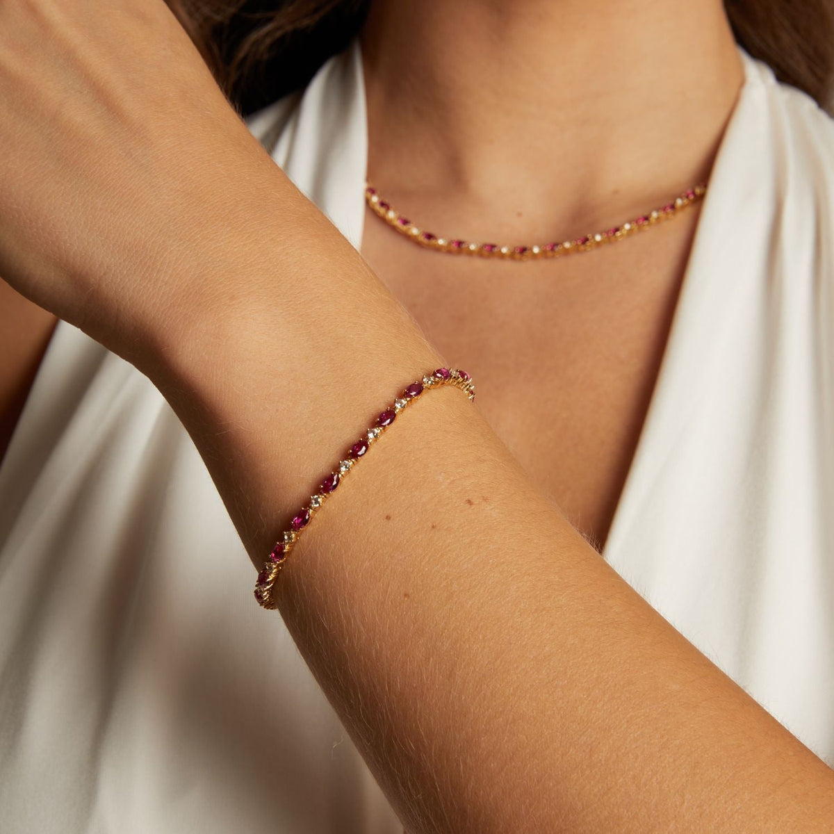 Model. Close-up of a person wearing a gold bracelet with red stones on a neutral background