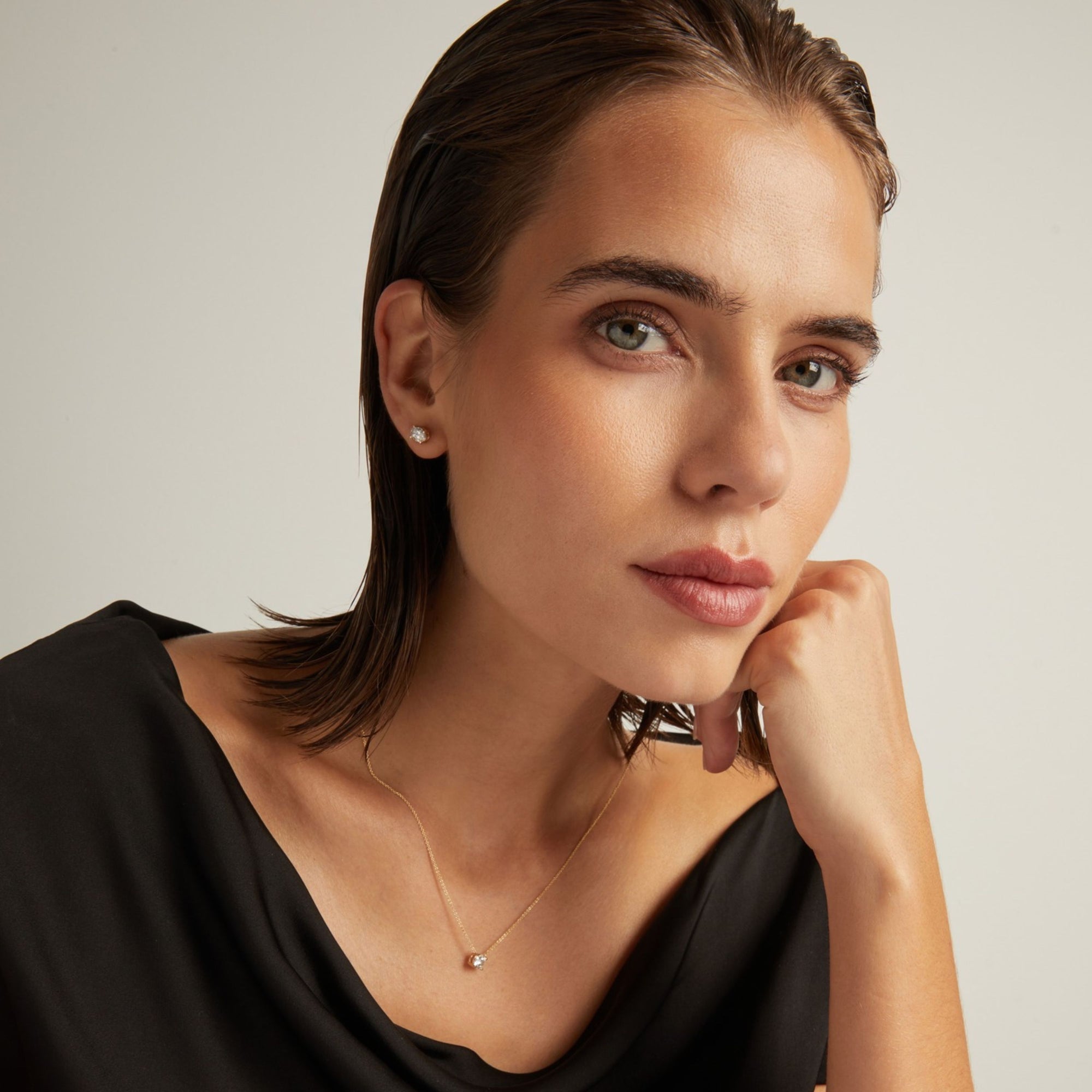 Model. Close up of woman wearing an oval diamond stud earring on a beige background.