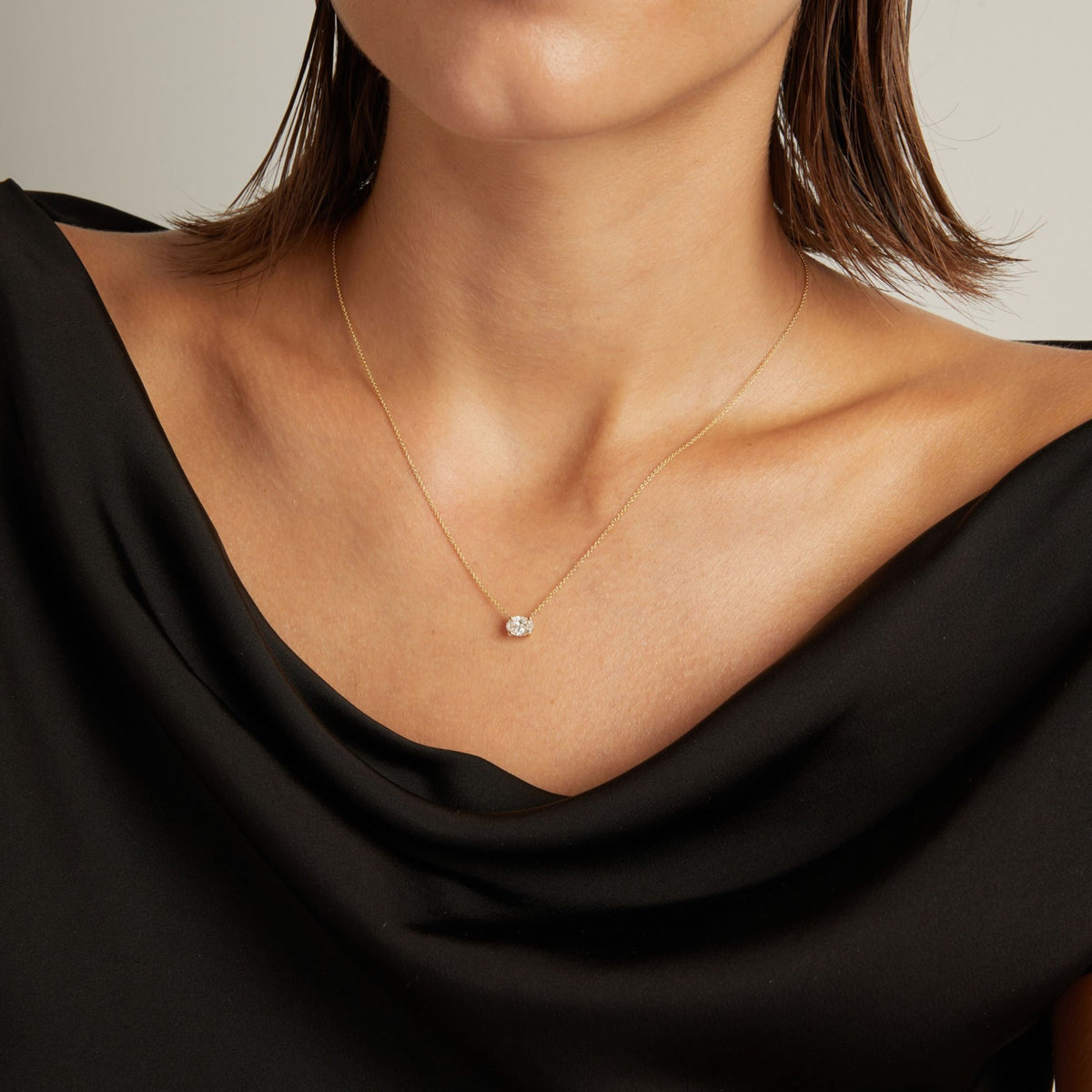 Model. Close up of woman wearing a black top with an oval diamond solitaire necklaces on a beige background.