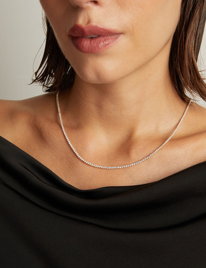 Model. Close up of a woman in a black top wearing a diamond tennis necklace on beige background.