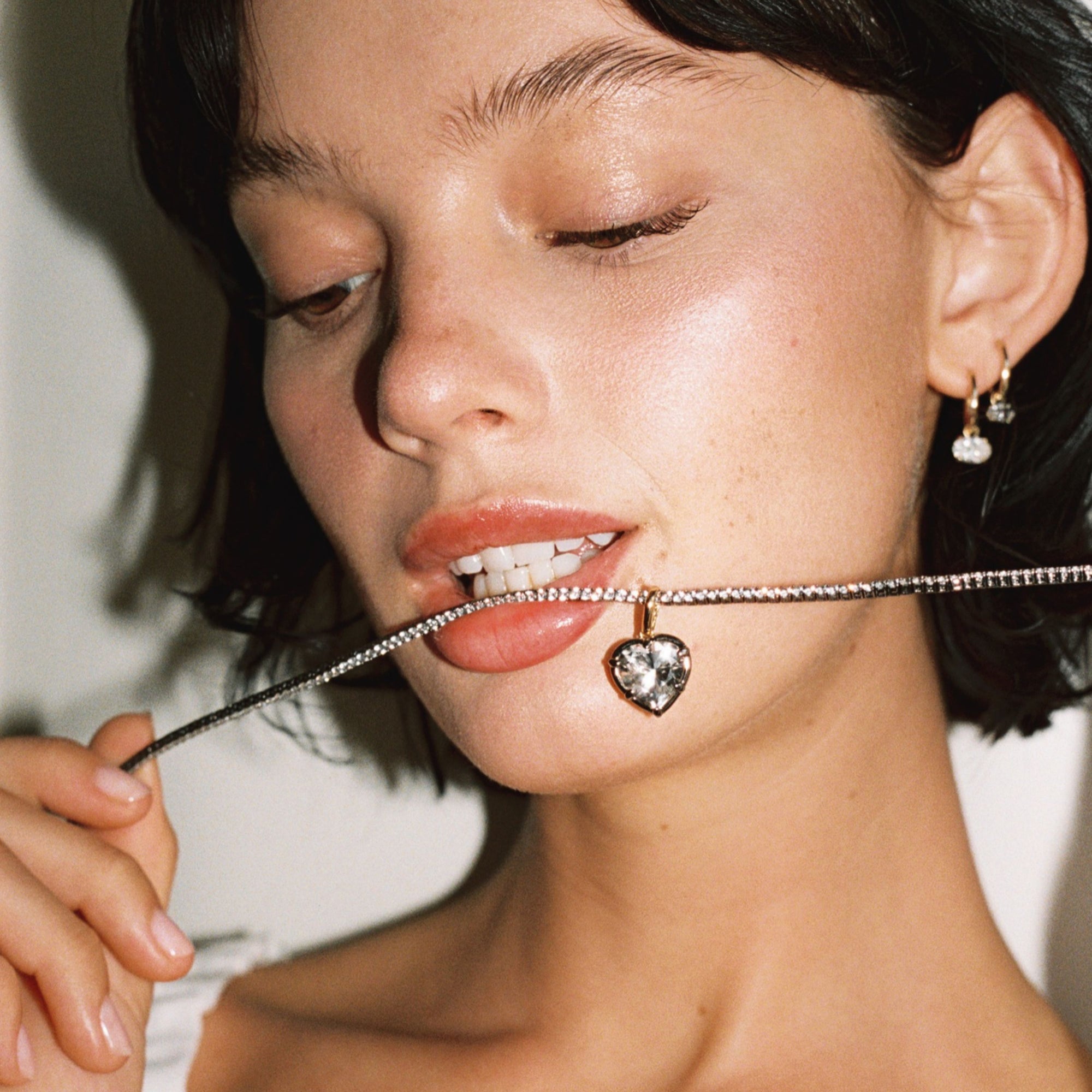 Model. Close up of woman with tennis necklace in mouth with heart gemstone pendant 