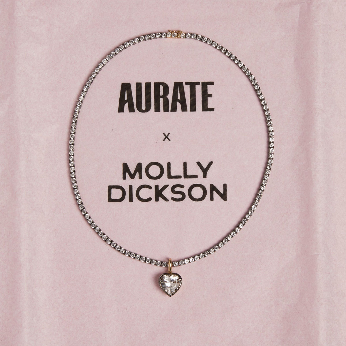 Model. Close up of black rhodium tennis necklace with heart shaped pendant on pink background.