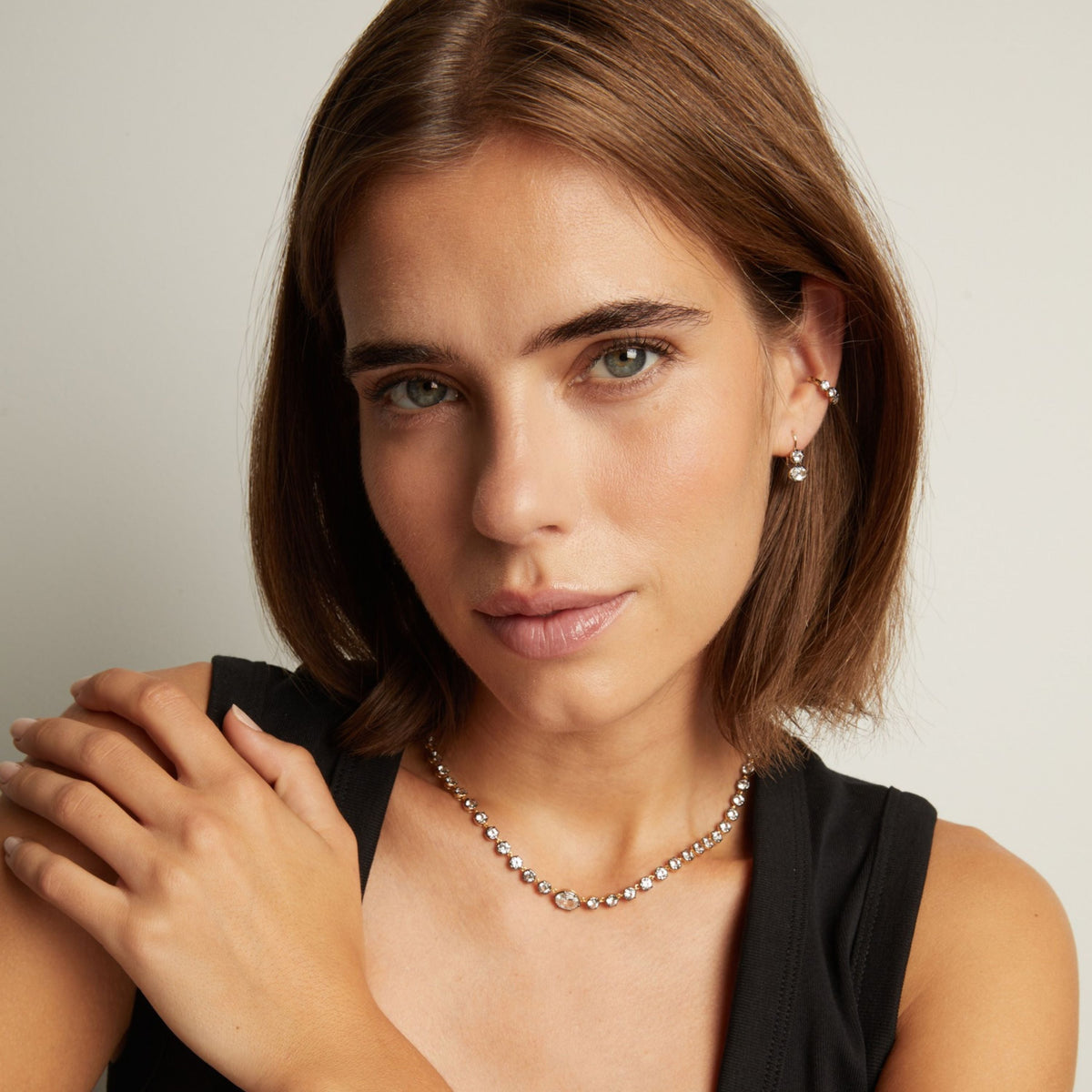 Model. Close up of woman wearing a couple gemstone earrings with a matching tennis necklace on neutral background.