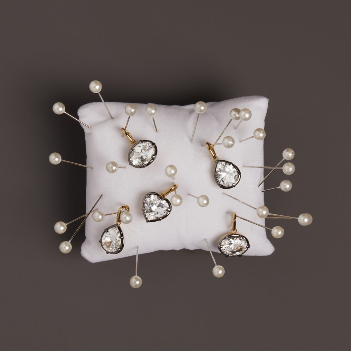 Model. Close up of black rhodium pendants on top on small white sewing pillow with sewing needles around it. 