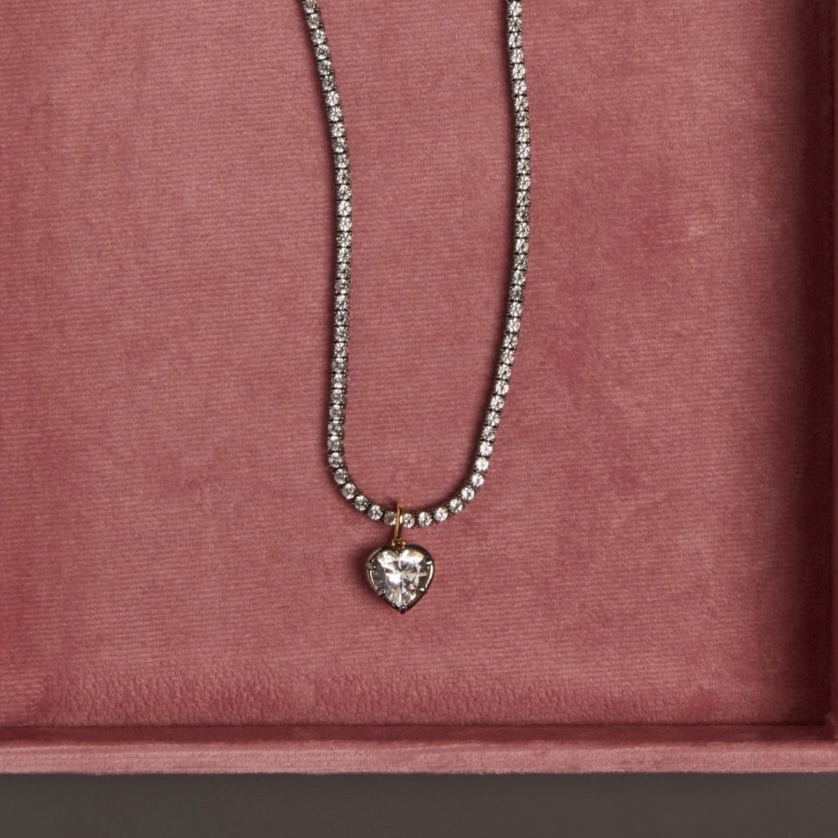 Model. Close up of black rhodium tennis necklace with heart shaped pendant on pink jewelry box.