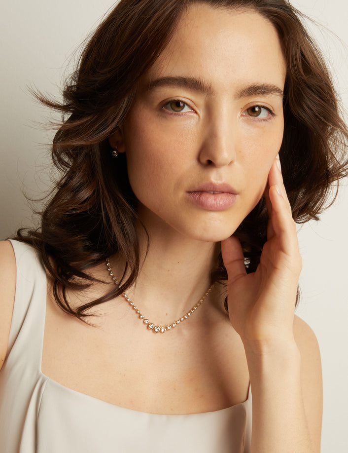 Woman wearing a diamond tennis necklace on a white background.