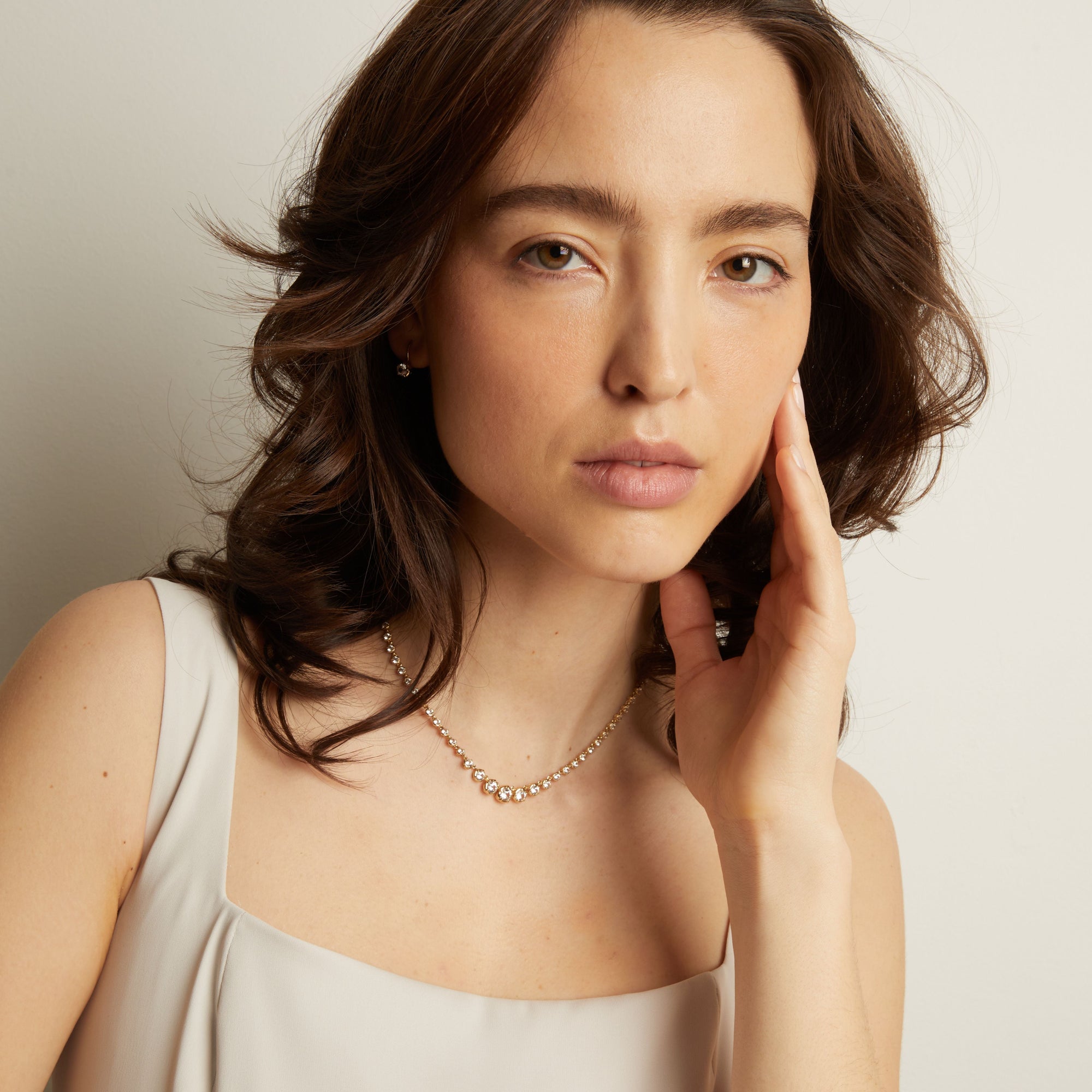Woman wearing a diamond tennis necklace on a white background.