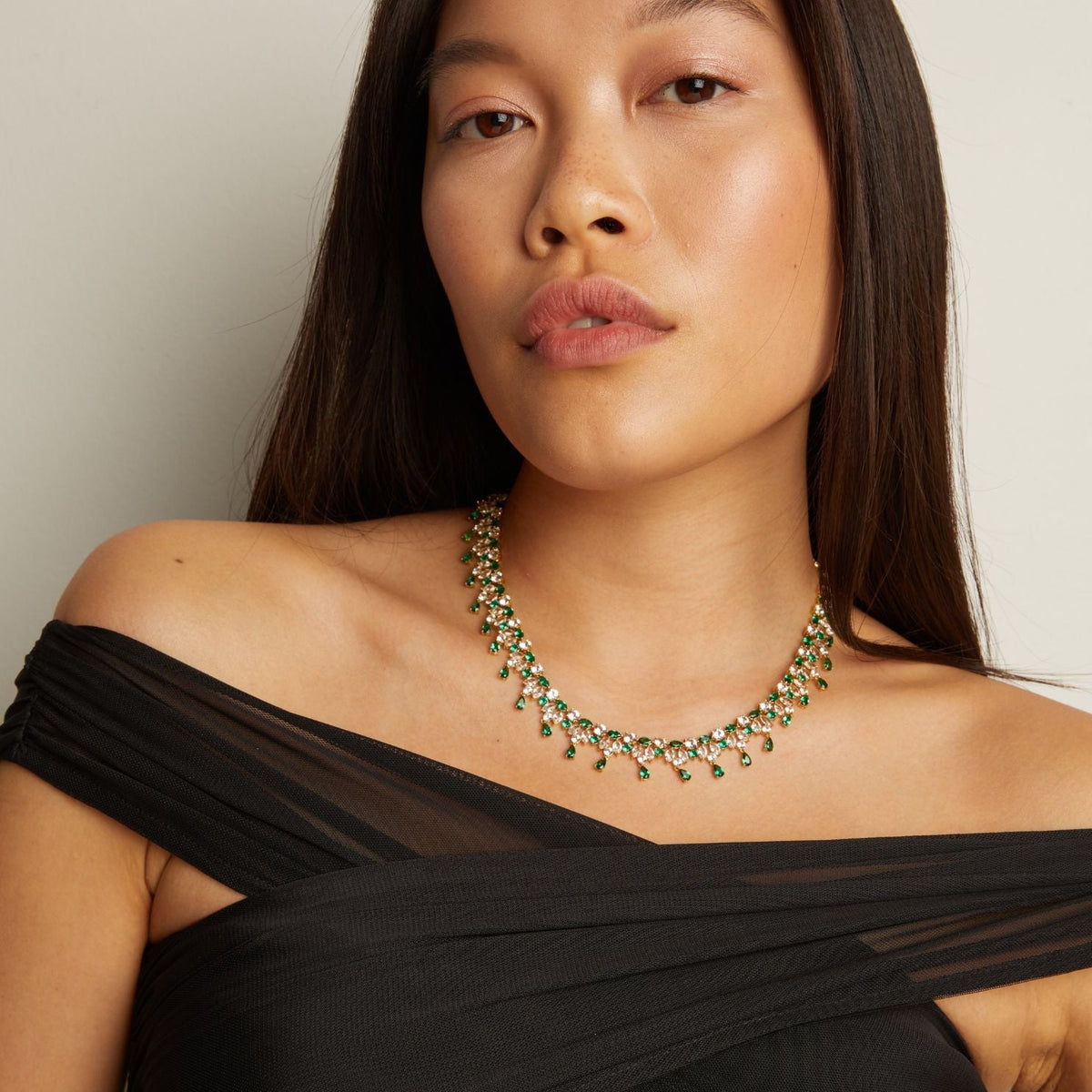 Model. Woman wearing a green emerald necklace against a neutral background