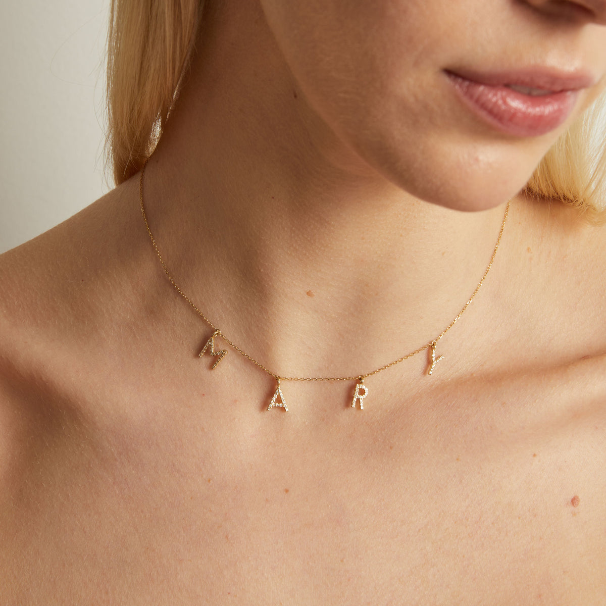 Model. Gold necklace with letter pendants on a person's neck