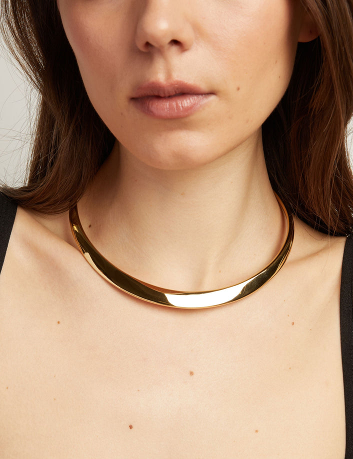 Close up of thick cold collar necklace on woman with neutral background.