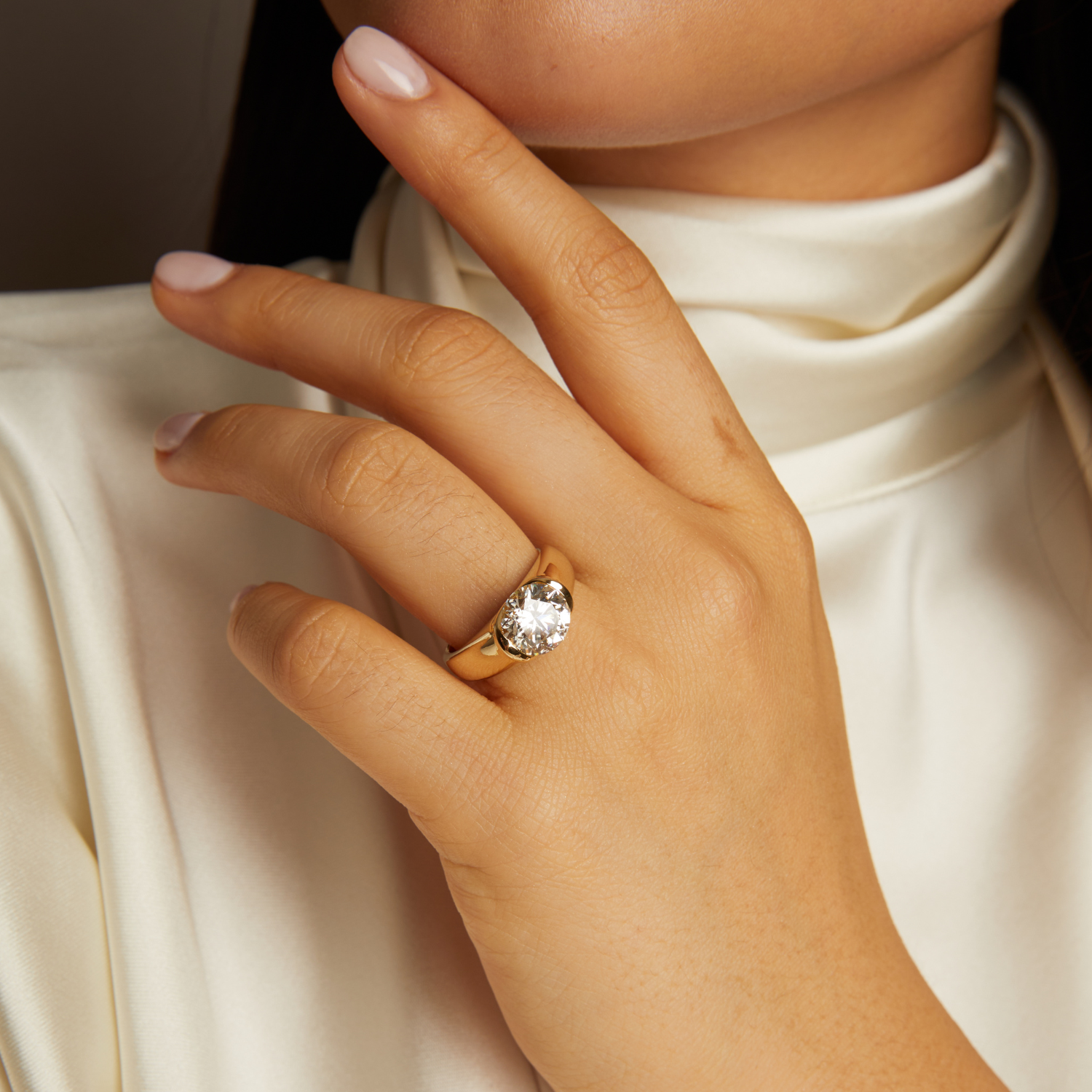 Close-up of a hand wearing a gold ring with a diamond on a neutral background