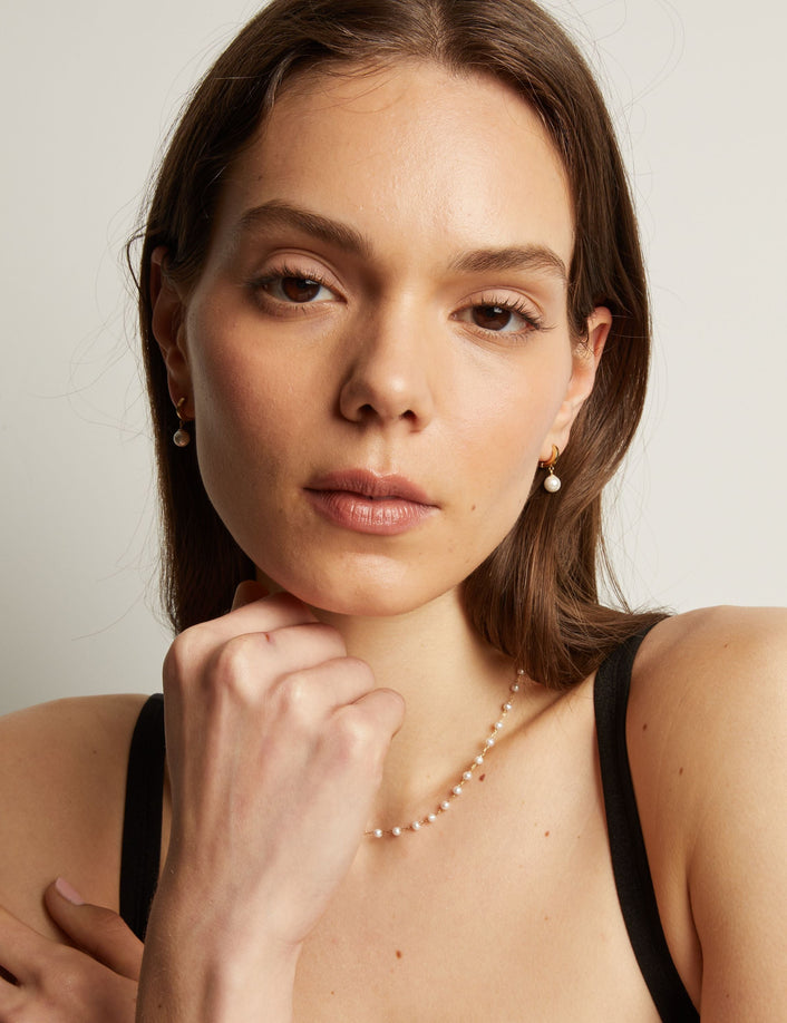 Model. Woman with pearl earring and necklace against a plain background.