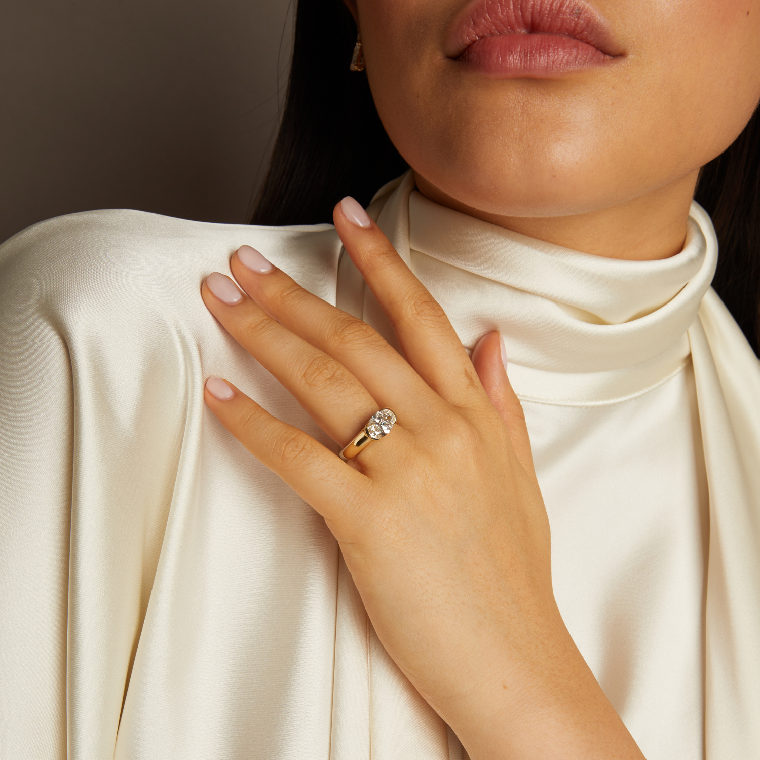 Close-up of a hand wearing a gold ring with a diamond, against a neutral background.