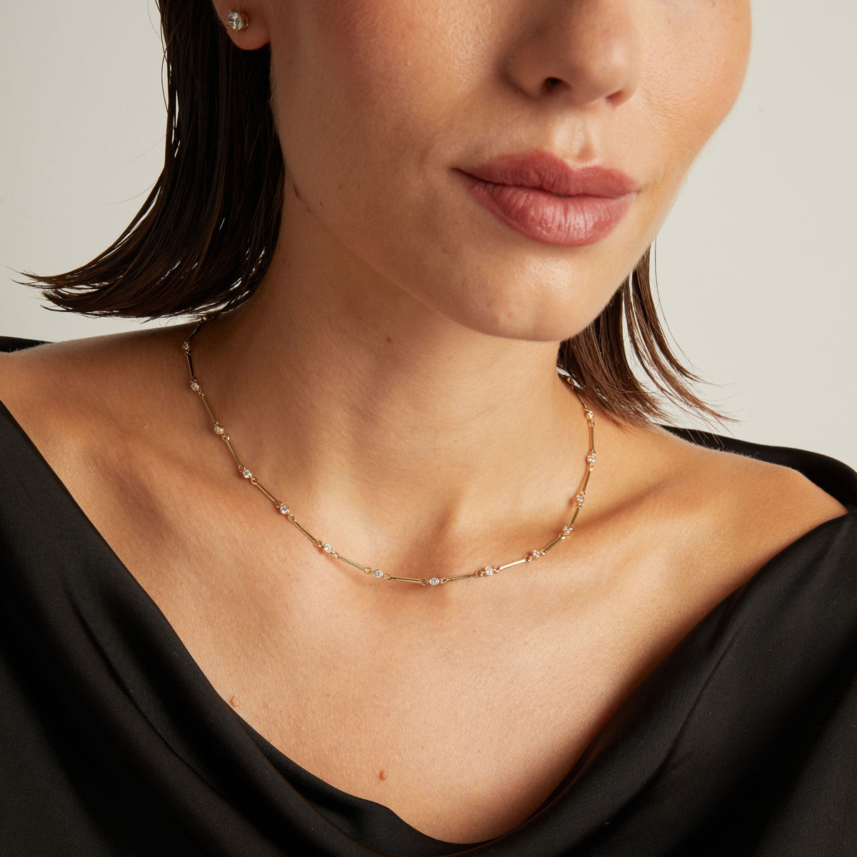 Model. Close up of a woman in a black top wearing a diamond bar necklace on beige background.