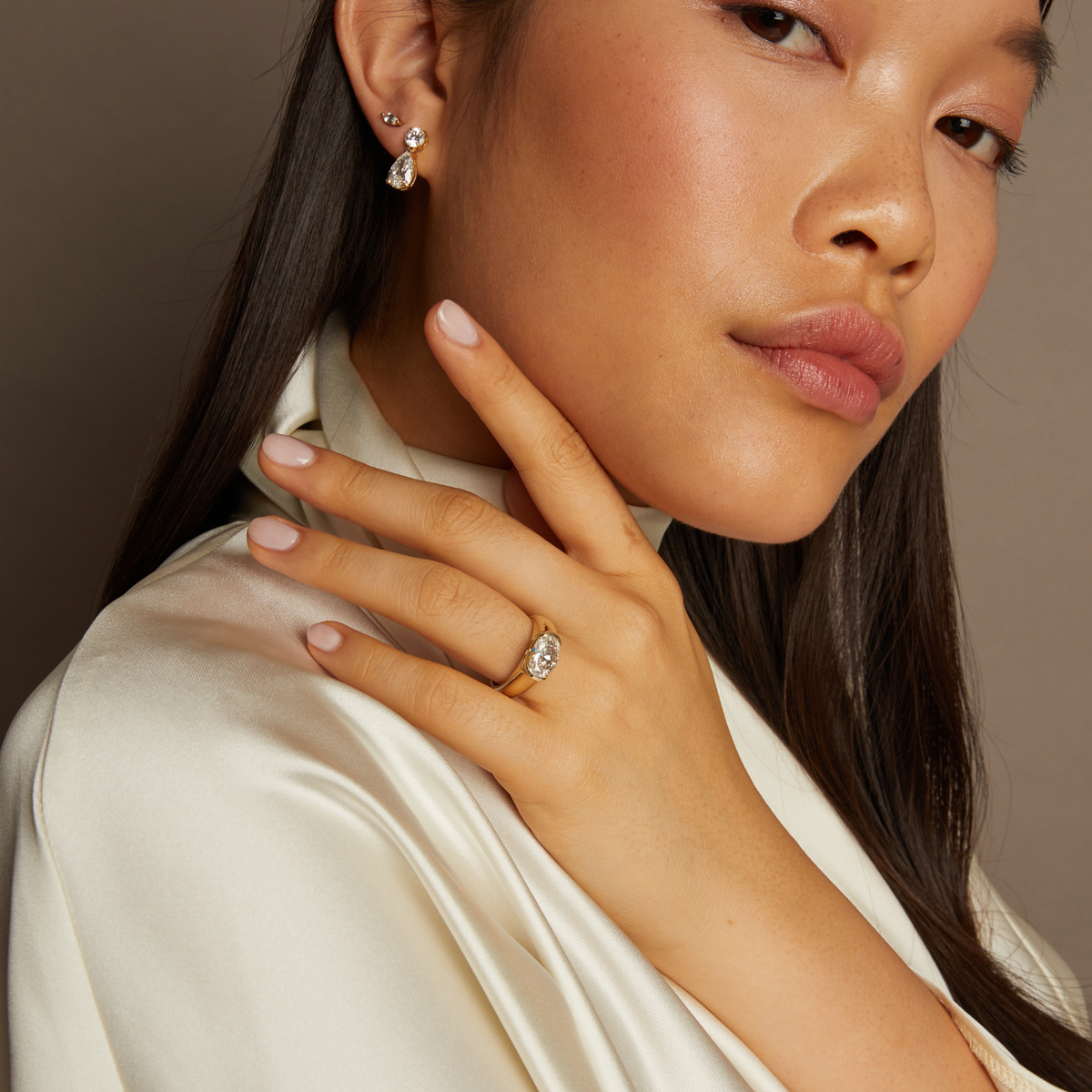 Model. Woman wearing diamond earrings and ring against a neutral background