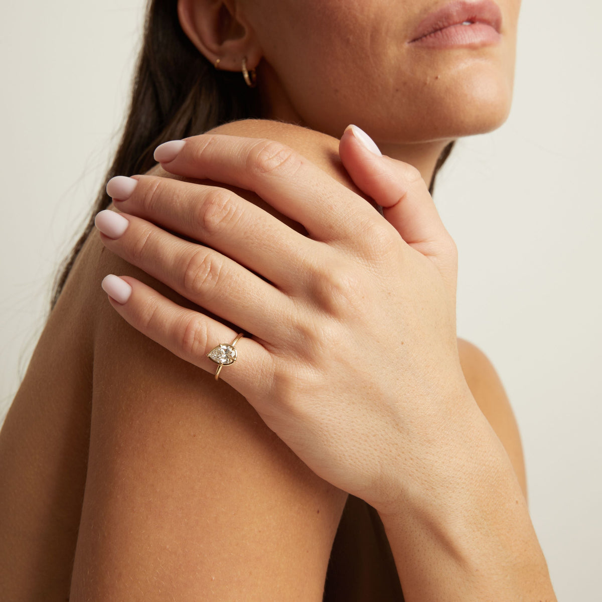 Model. A close-up lifestyle shot of a woman wearing a delicate gold ring with a pear diamond. 