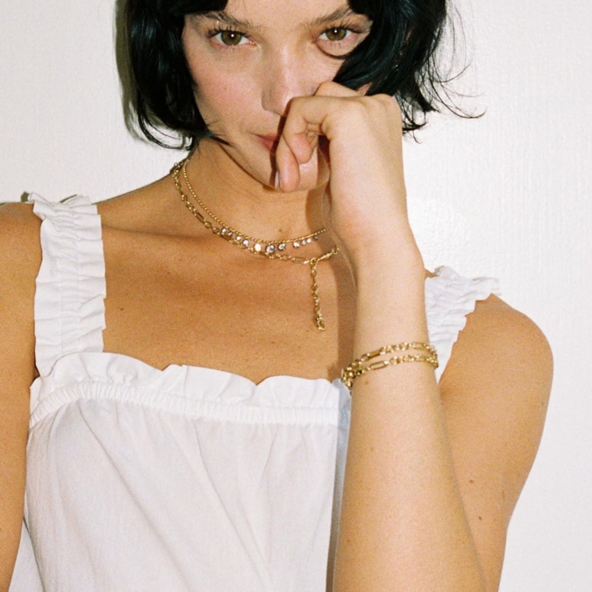 Model. Close up of woman wearing stacked gold chain bracelets and stacked chain necklaces on white background. 
