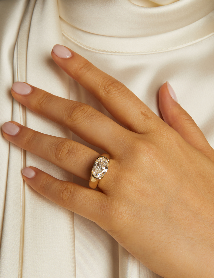 Hand wearing a gold ring with a diamond on a beige background