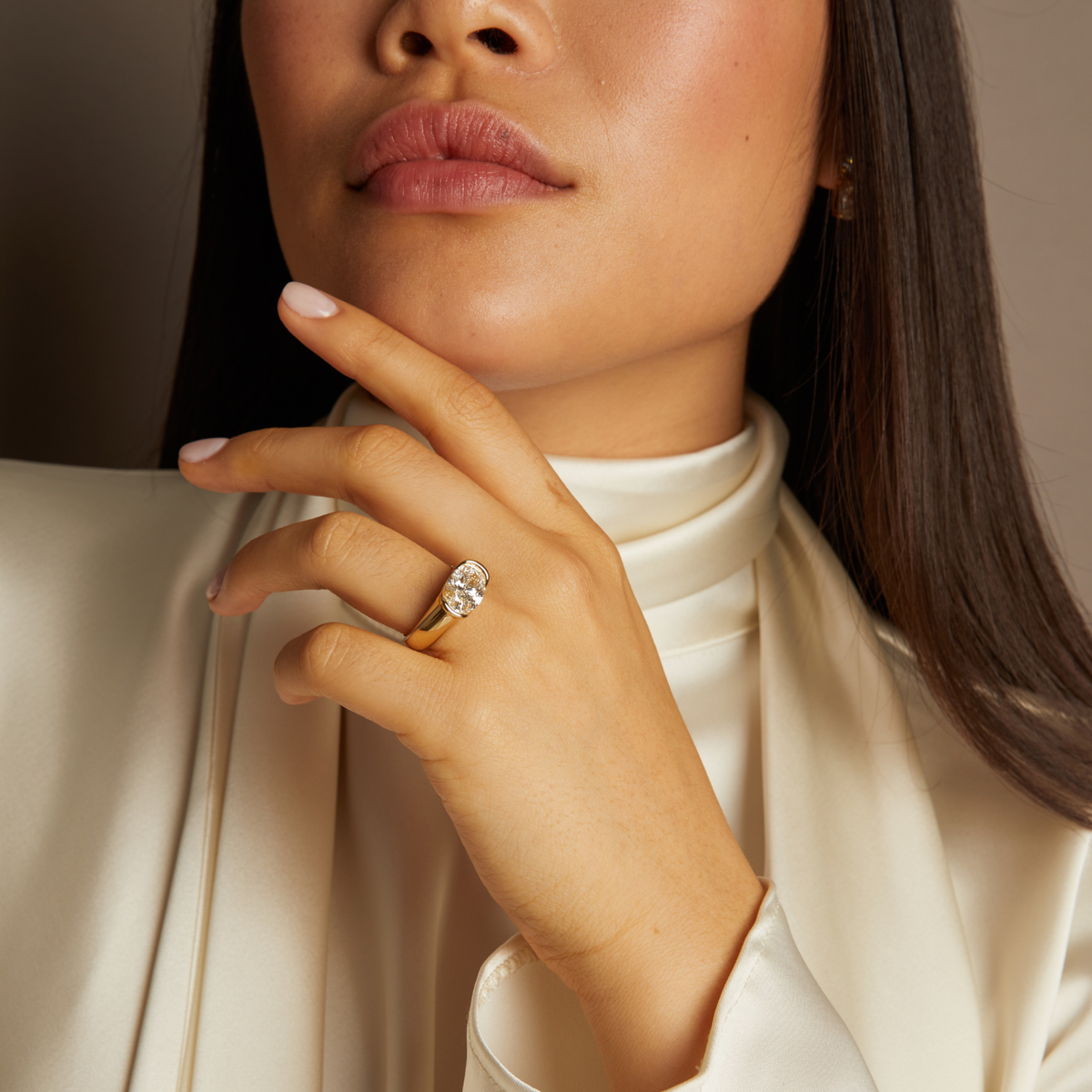 Model. Close-up of a woman wearing a diamond ring on her finger, with a neutral background.