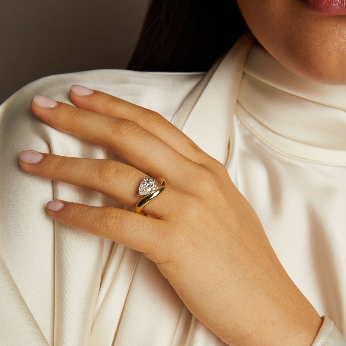 Hand wearing a gold ring with a diamond on a neutral background