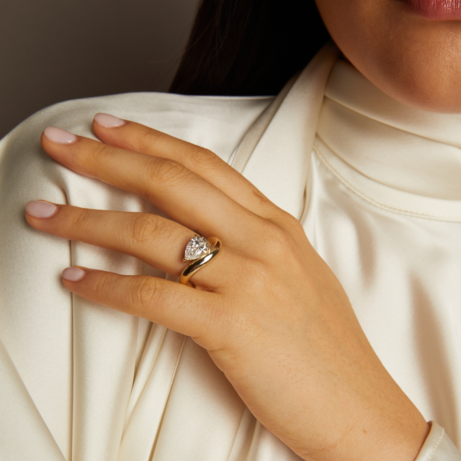 Hand wearing a gold ring with a diamond on a neutral background