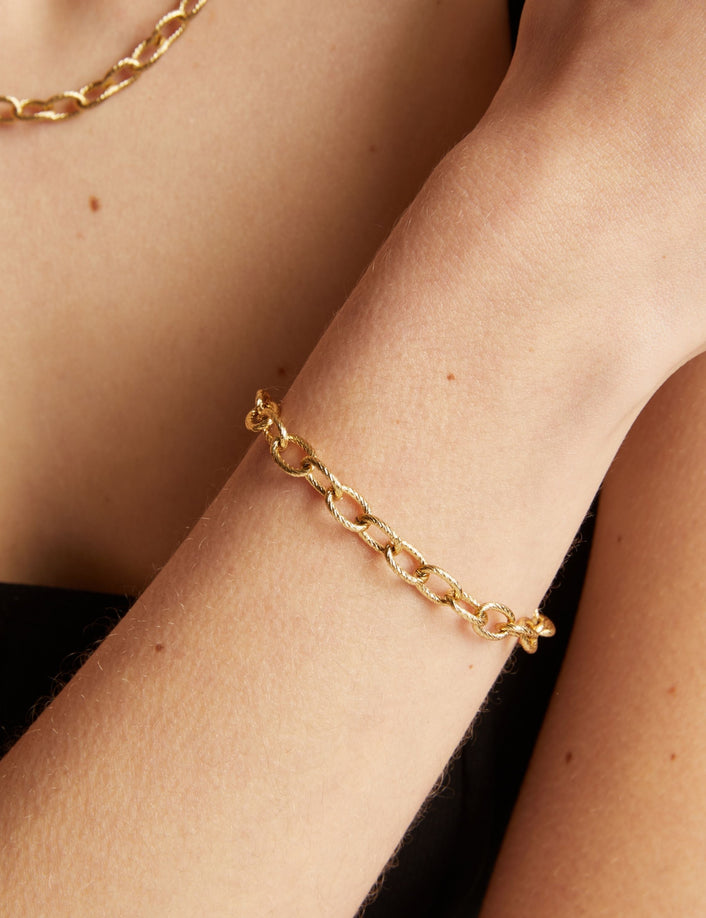 Gold chain bracelet on a wrist with a neutral background.