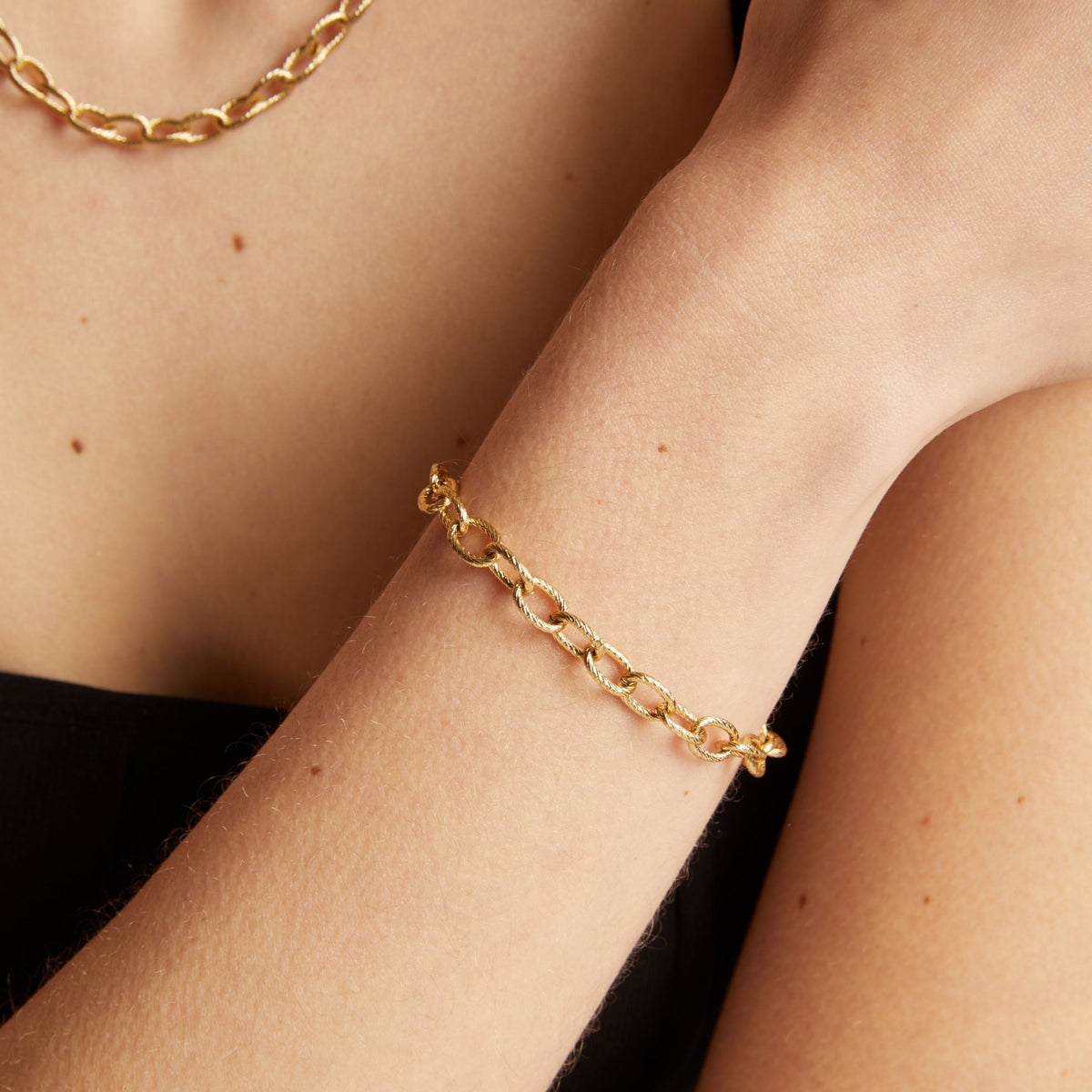 Gold chain bracelet on a wrist with a neutral background.