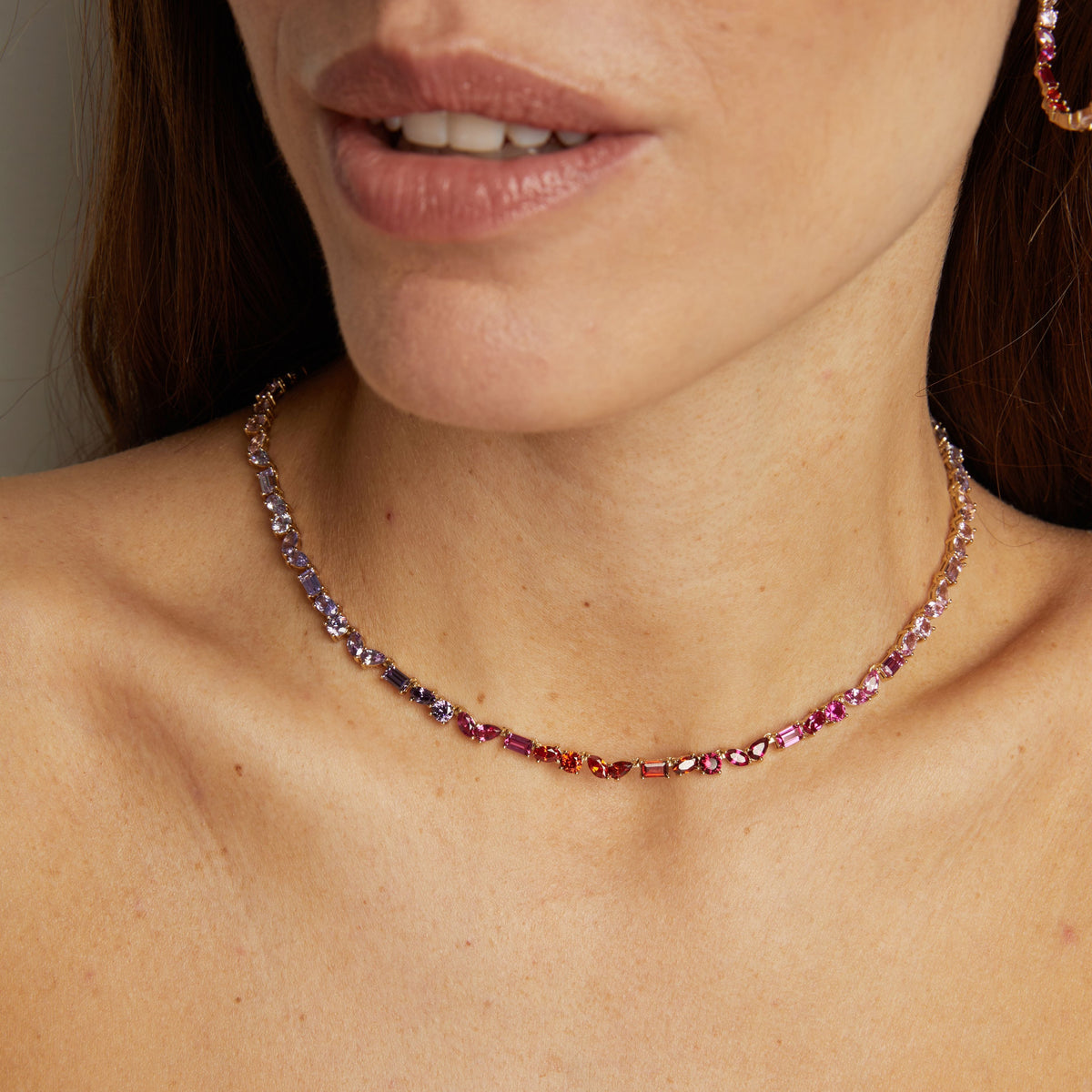 Model. Close-up of a woman wearing a delicate necklace with pink gemstones.