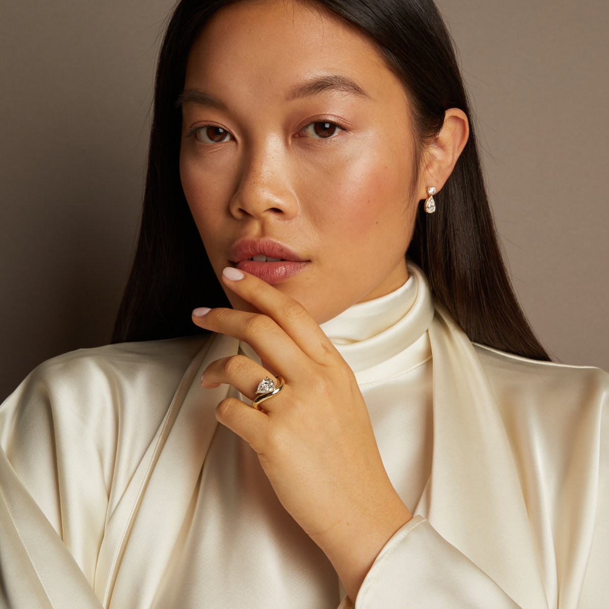 Model. Woman wearing a white turtleneck and gold jewelry against a neutral background