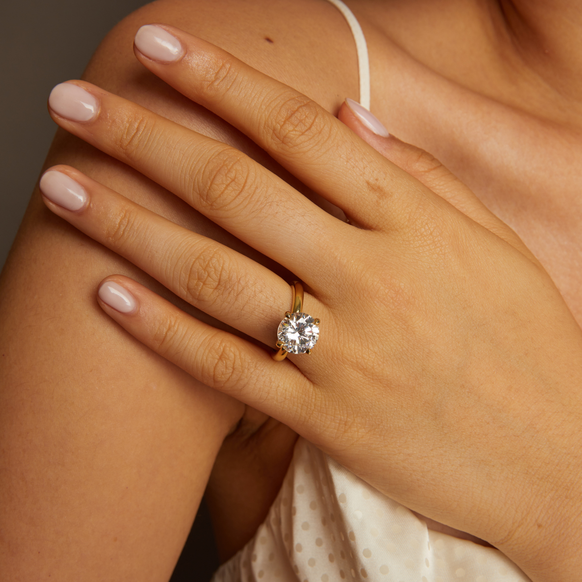 Model. Close-up of a hand wearing a diamond ring on a neutral background
