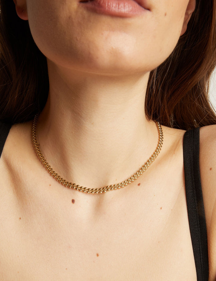 Close up of a person wearing a gold chain necklace against a neutral background.