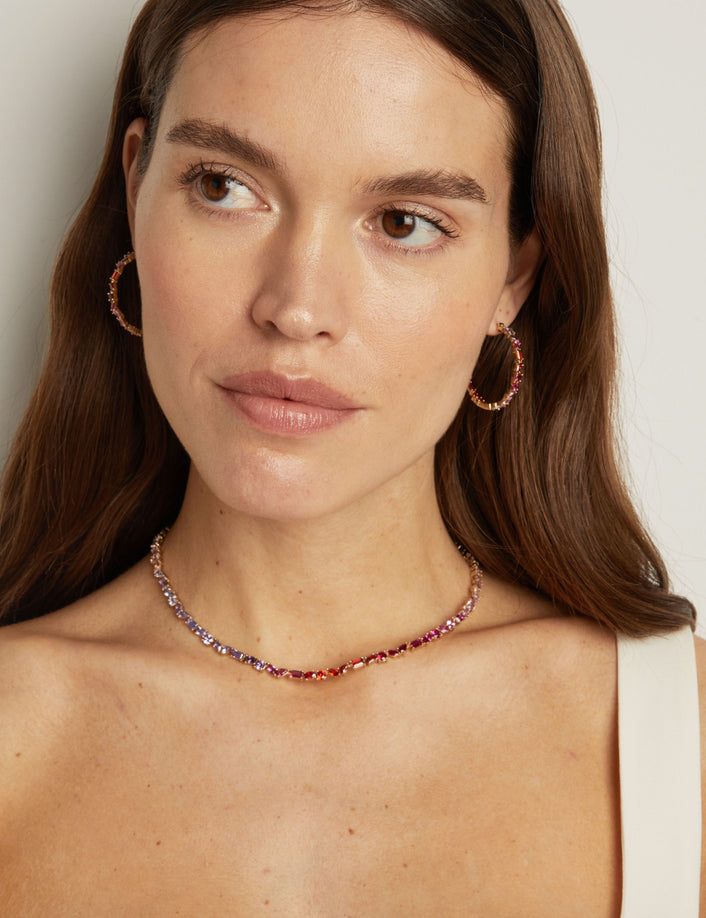 Model. Woman wearing a necklace and hoop earrings against a neutral background
