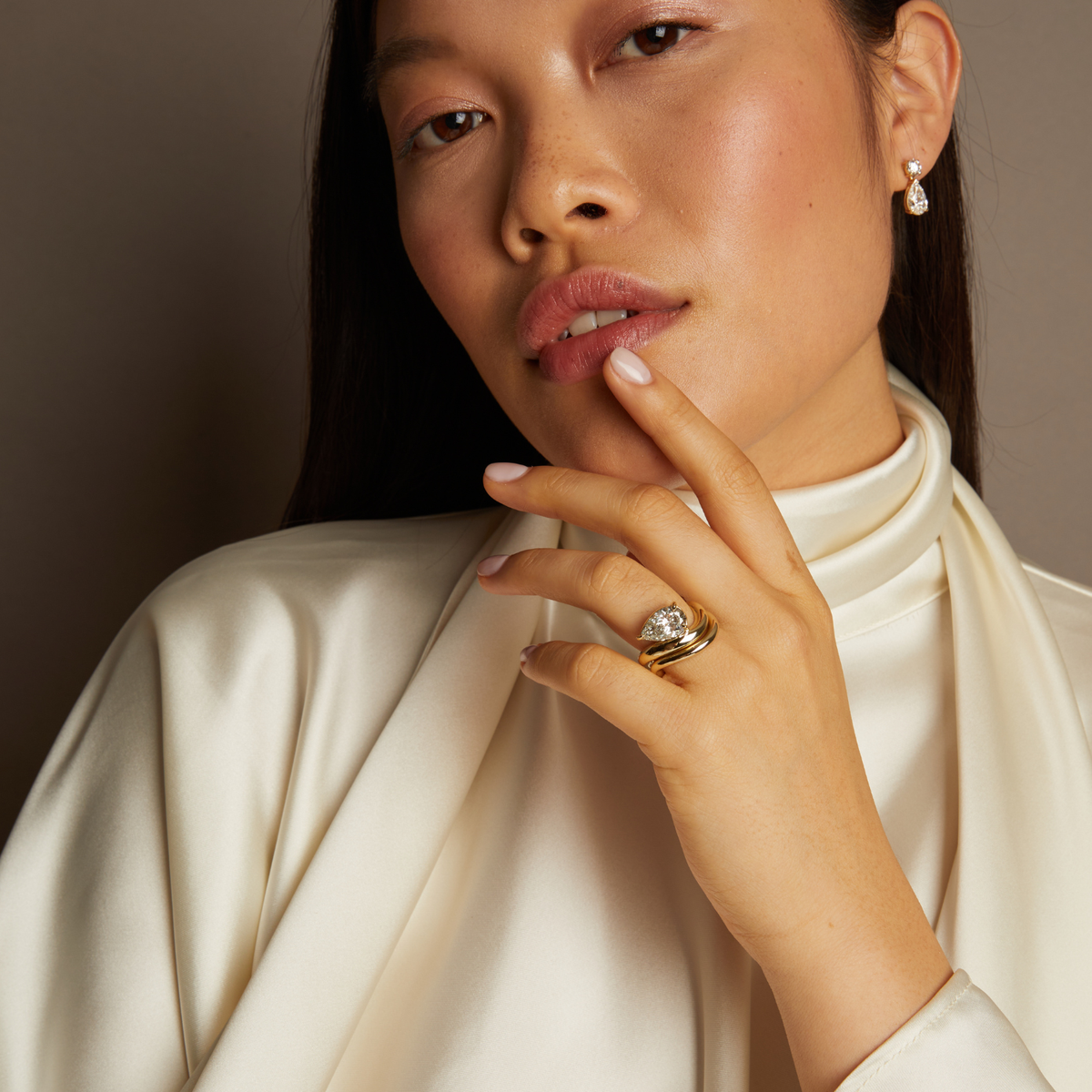 Model. Woman wearing a gold ring with a diamond, posing with hand near face.