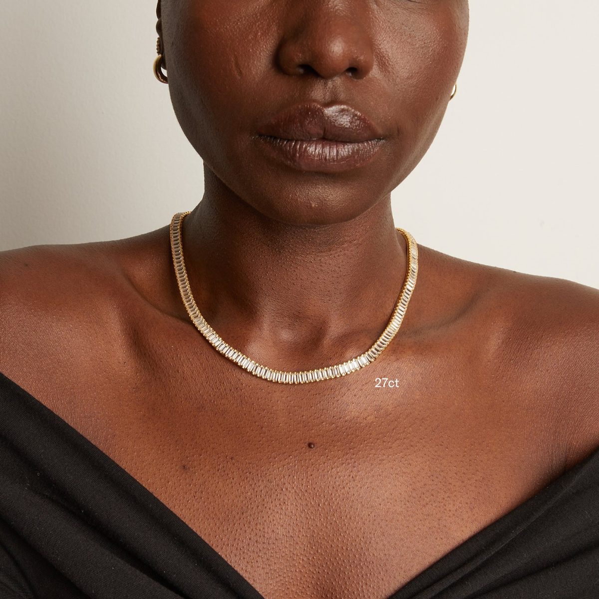 Model. Woman wearing a gold necklace on a neutral background