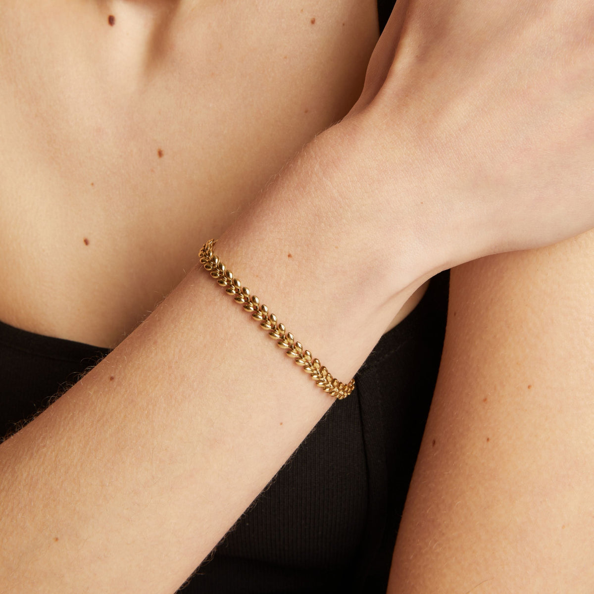 Gold chain bracelet on a person's wrist with a neutral background