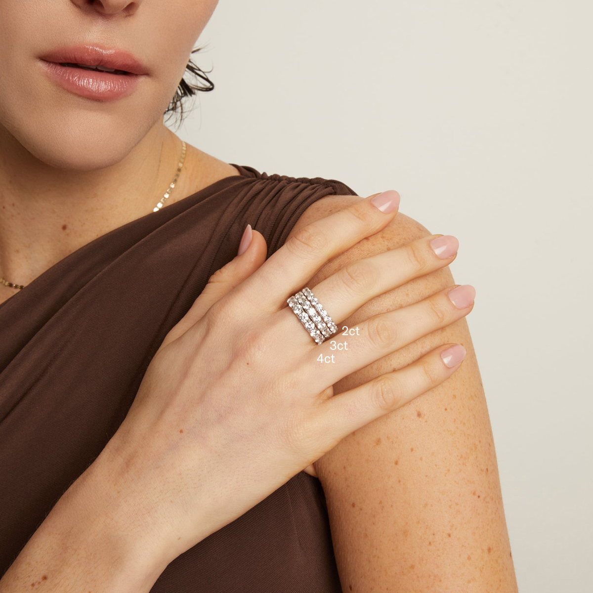 Model. Close-up of a woman's hand wearing a silver ring with diamond accents on a neutral background