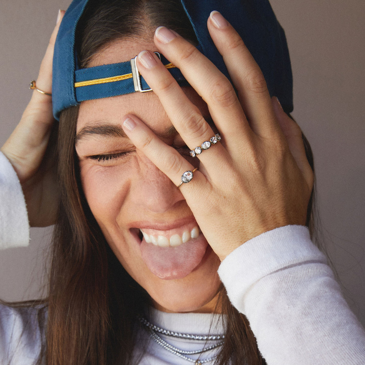 Model. Close up of woman wearing two rings with her hand over her face and tongue out. 