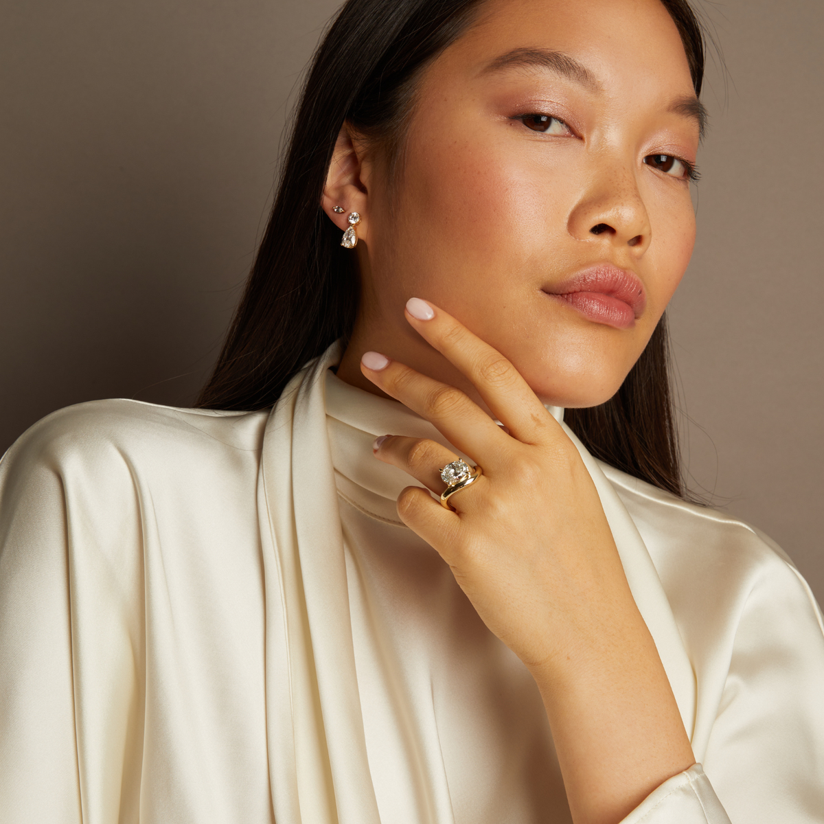 Model. Woman wearing jewelry including earrings and a ring, with a neutral background