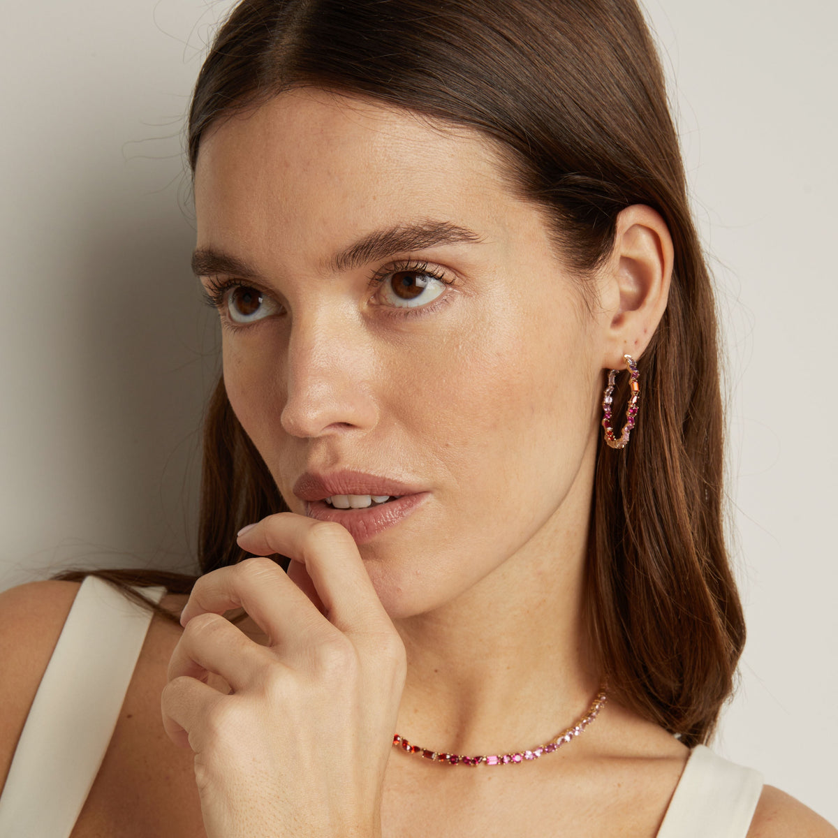 Model. Woman wearing pink hoop earrings and a matching necklace against a neutral background